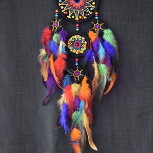 May include: A colorful dreamcatcher with three black hoops decorated with beads and colorful feathers. The hoops are embroidered with a starburst pattern.