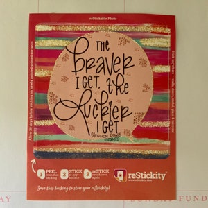 May include: A pink and gold sticker with the quote "The braver I get, the luckier I get" by Glennon Doyle. The sticker has a colourful striped background and a leopard print design.