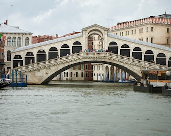 Puede incluir: Un puente de piedra blanca con arcos sobre un canal en Venecia, Italia. La gente camina por el puente.