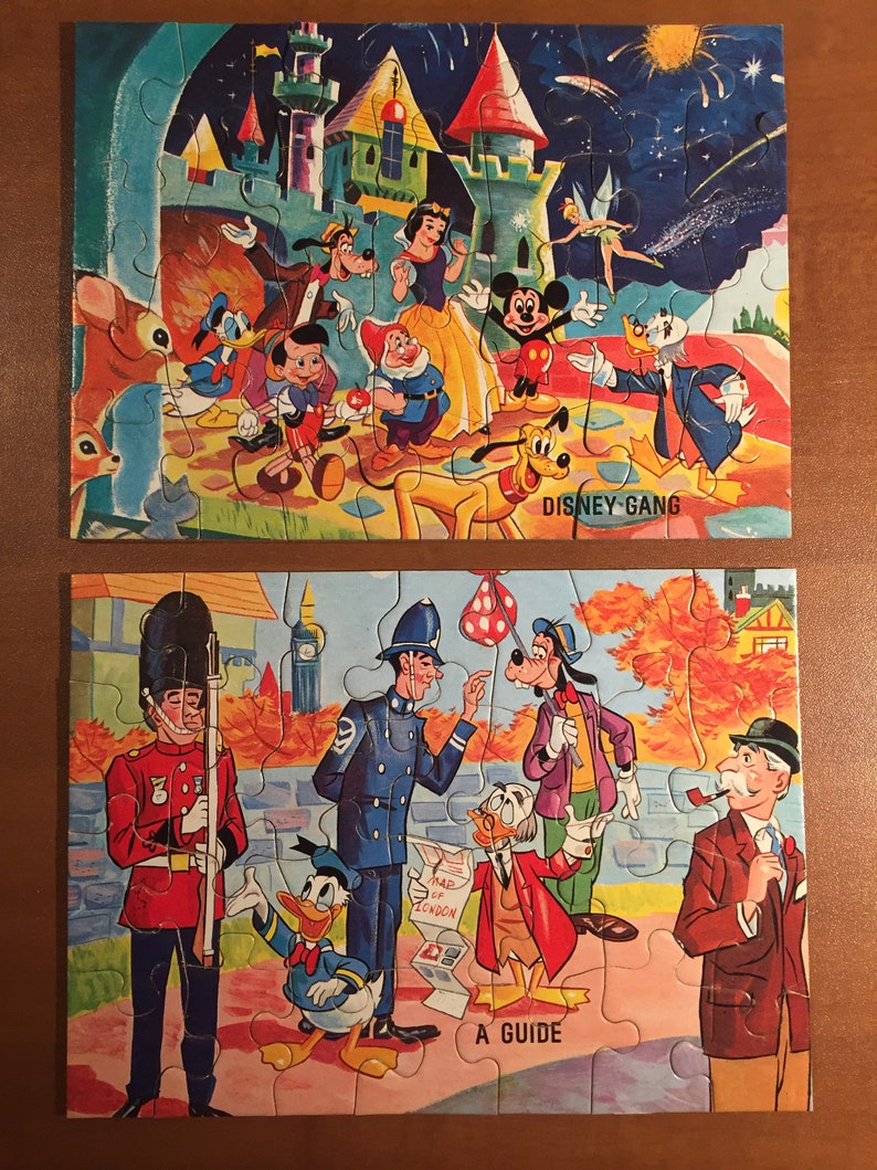 May include: Two vintage jigsaw puzzles featuring Disney characters. The first puzzle shows Mickey Mouse, Donald Duck, Goofy, Snow White, and other Disney characters in front of a castle. The second puzzle shows Mickey Mouse, Donald Duck, Goofy, and other Disney characters in front of a building with a sign that says "A Guide".