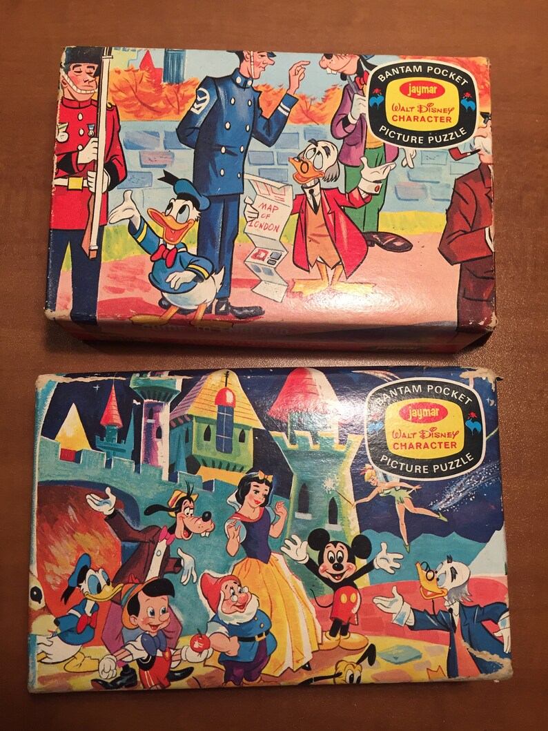 May include: Two vintage Walt Disney character picture puzzles in their original boxes. The top box features Donald Duck, a British policeman, and a man with a map of London. The bottom box features Mickey Mouse, Snow White, and other Disney characters.