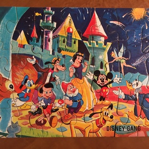 May include: A vintage Disney jigsaw puzzle featuring Mickey Mouse, Minnie Mouse, Donald Duck, Goofy, Pluto, Snow White, and the Seven Dwarfs. The puzzle depicts the characters in front of a castle with fireworks in the background. The puzzle is titled "Disney Gang".