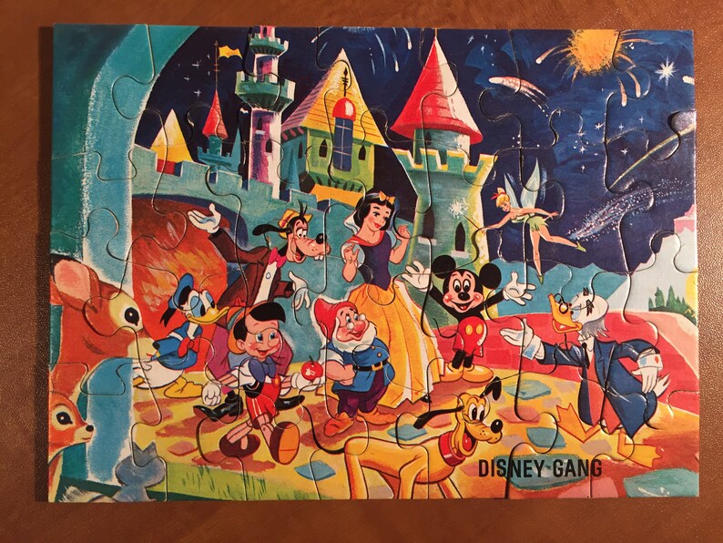 May include: A vintage Disney jigsaw puzzle featuring Mickey Mouse, Minnie Mouse, Donald Duck, Goofy, Pluto, Snow White, and the Seven Dwarfs. The puzzle depicts the characters in front of a castle with fireworks in the background. The puzzle is titled "Disney Gang".