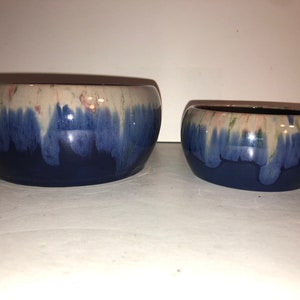 Puede incluir: Dos cuencos de cerámica azul y blanco con un acabado esmaltado. El cuenco más grande está en el fondo y el más pequeño está en primer plano.