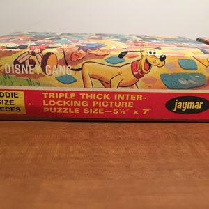 May include: A vintage cardboard box for a Disney character jigsaw puzzle. The box features a colorful illustration of Mickey Mouse, Donald Duck, Goofy, and Pluto. The text on the box reads "The Disney Gang" and "Triple Thick Inter-Locking Picture Puzzle Size - 5 1/2" x 7"  Kiddie Size Pieces Jaymar 8741".