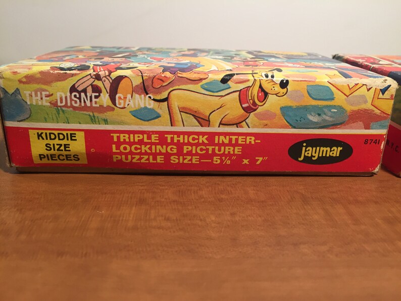 May include: A vintage cardboard box for a Disney character jigsaw puzzle. The box features a colorful illustration of Mickey Mouse, Donald Duck, Goofy, and Pluto. The text on the box reads "The Disney Gang" and "Triple Thick Inter-Locking Picture Puzzle Size - 5 1/2" x 7"  Kiddie Size Pieces Jaymar 8741".