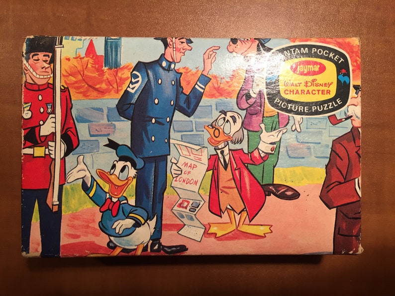 May include: A vintage cardboard box for a Walt Disney character picture puzzle. The box features a colorful illustration of Donald Duck, a policeman, a man with a pipe, and a man holding a map of London. The box is labeled "Jaymar Bantam Pocket Walt Disney Character Picture Puzzle".