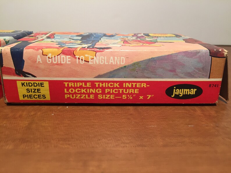 May include: A red and white cardboard box for a "A Guide to England" jigsaw puzzle. The box features a picture of a cartoon scene with a red and white striped background. The box is labeled "Triple Thick Inter-Locking Picture" and "Kiddie Size Pieces". The puzzle size is 5 1/2 inches by 7 inches. The box is labeled "Jaymar" and has the number 8741 printed on it.