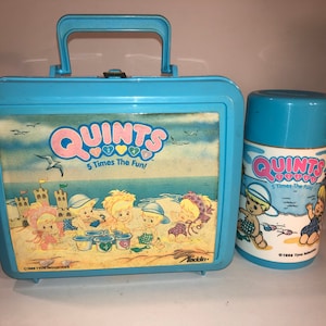 Puede incluir: Una fiambrera y un termo de plástico azul con una escena de playa y las palabras "Quints 5 Times The Fun!" en ellos.