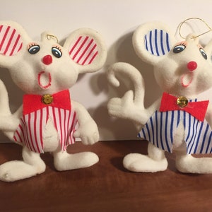 May include: Two white felt mouse ornaments with red and blue striped shirts and bow ties. The mouse on the left has a red and white striped shirt and the mouse on the right has a blue and white striped shirt.
