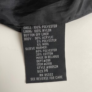Puede incluir: Una etiqueta de prenda negra con texto blanco que detalla la composici&oacute;n de la tela: exterior 100% poli&eacute;ster, forro 100% nailon y un forro desmontable. El cuerpo es 90% acr&iacute;lico, 5% poli&eacute;ster y 5% lana. Talla 14.
