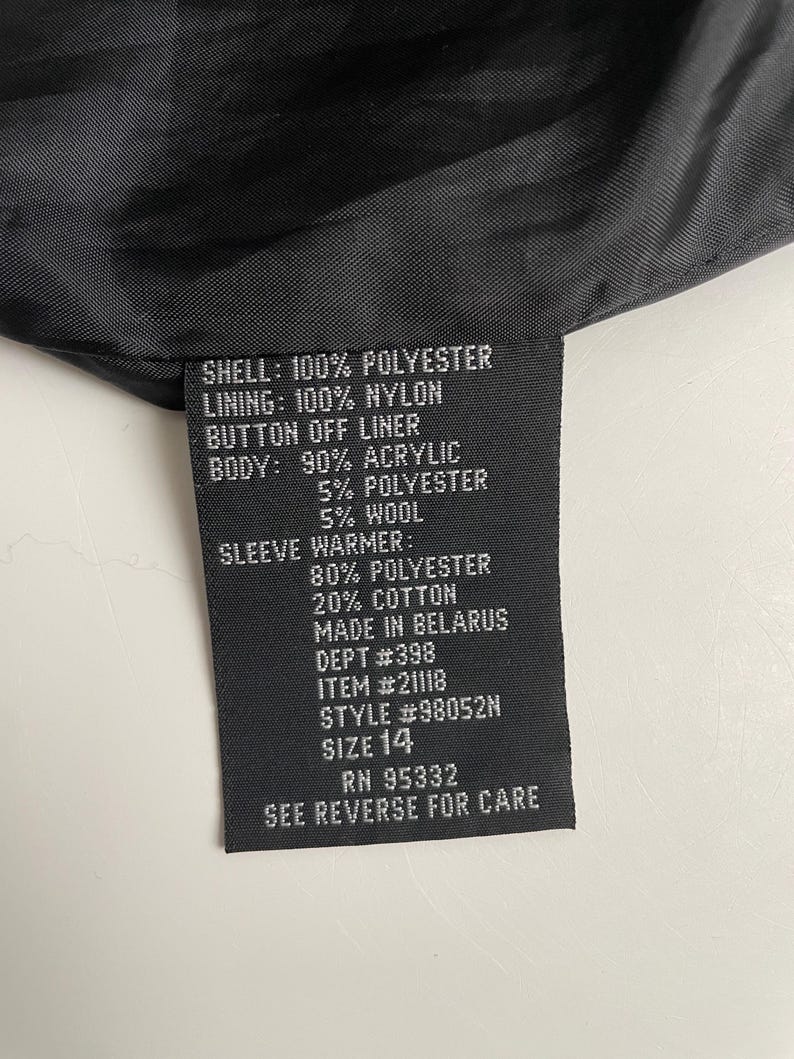 Puede incluir: Una etiqueta de prenda negra con texto blanco que detalla la composici&oacute;n de la tela: exterior 100% poli&eacute;ster, forro 100% nailon y un forro desmontable. El cuerpo es 90% acr&iacute;lico, 5% poli&eacute;ster y 5% lana. Talla 14.