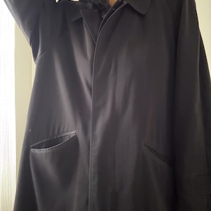 Puede incluir: Un abrigo tipo trench negro con cuello cl&aacute;sico y dos bolsillos delanteros. El abrigo tiene un dise&ntilde;o largo y fluido y est&aacute; hecho de una tela oscura y lisa. Las mangas tienen un detalle de pu&ntilde;o. Una prenda de abrigo atemporal.