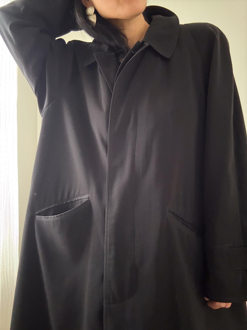 Puede incluir: Un abrigo tipo trench negro con cuello cl&aacute;sico y dos bolsillos delanteros. El abrigo tiene un dise&ntilde;o largo y fluido y est&aacute; hecho de una tela oscura y lisa. Las mangas tienen un detalle de pu&ntilde;o. Una prenda de abrigo atemporal.