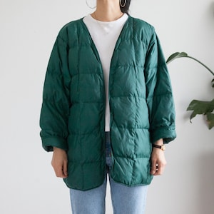 May include: A long, dark green quilted jacket with a v-neck and button closure. The jacket has a relaxed fit and is made of a soft, comfortable material.