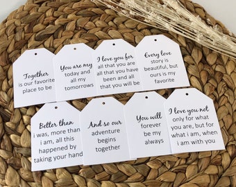 Può includere: Otto etichette regalo bianche con testo nero. Le etichette presentano citazioni romantiche sull'amore e le relazioni. Le etichette sono disposte su una superficie intrecciata marrone.