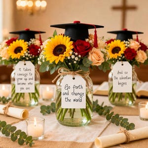 May include: Three graduation-themed floral arrangements in glass jars. Each arrangement features a black mortarboard hat, sunflowers, red roses, and other flowers. The jars have tags with inspirational quotes. Candles and rolled diplomas are also present.