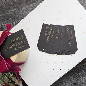 May include: Black gift tags with gold lettering that reads "Merry Christmas" and "The Maymoms". The tags are on a white background with gold polka dots.
