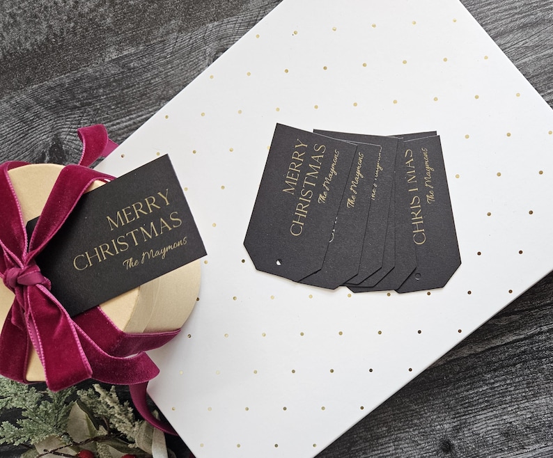May include: Black gift tags with gold lettering that reads "Merry Christmas" and "The Maymoms". The tags are on a white background with gold polka dots.