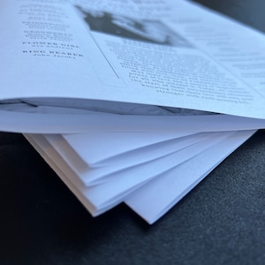 May include: A stack of white paper sheets, likely for a wedding or event. The top sheet is curved, revealing the text of the document. The text includes names and titles such as "Flower Girl" and "Ring Bearer".