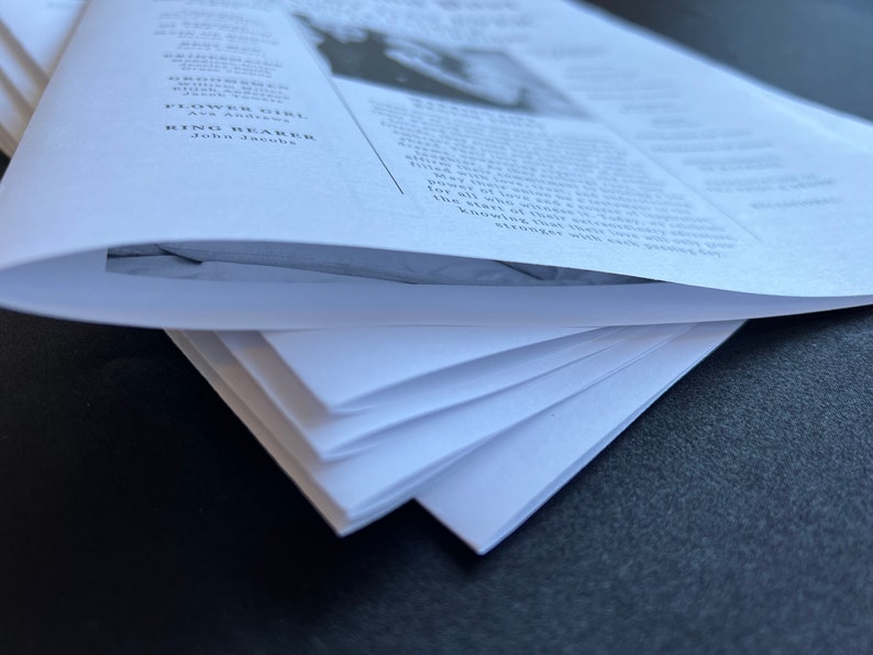 May include: A stack of white paper sheets, likely for a wedding or event. The top sheet is curved, revealing the text of the document. The text includes names and titles such as "Flower Girl" and "Ring Bearer".