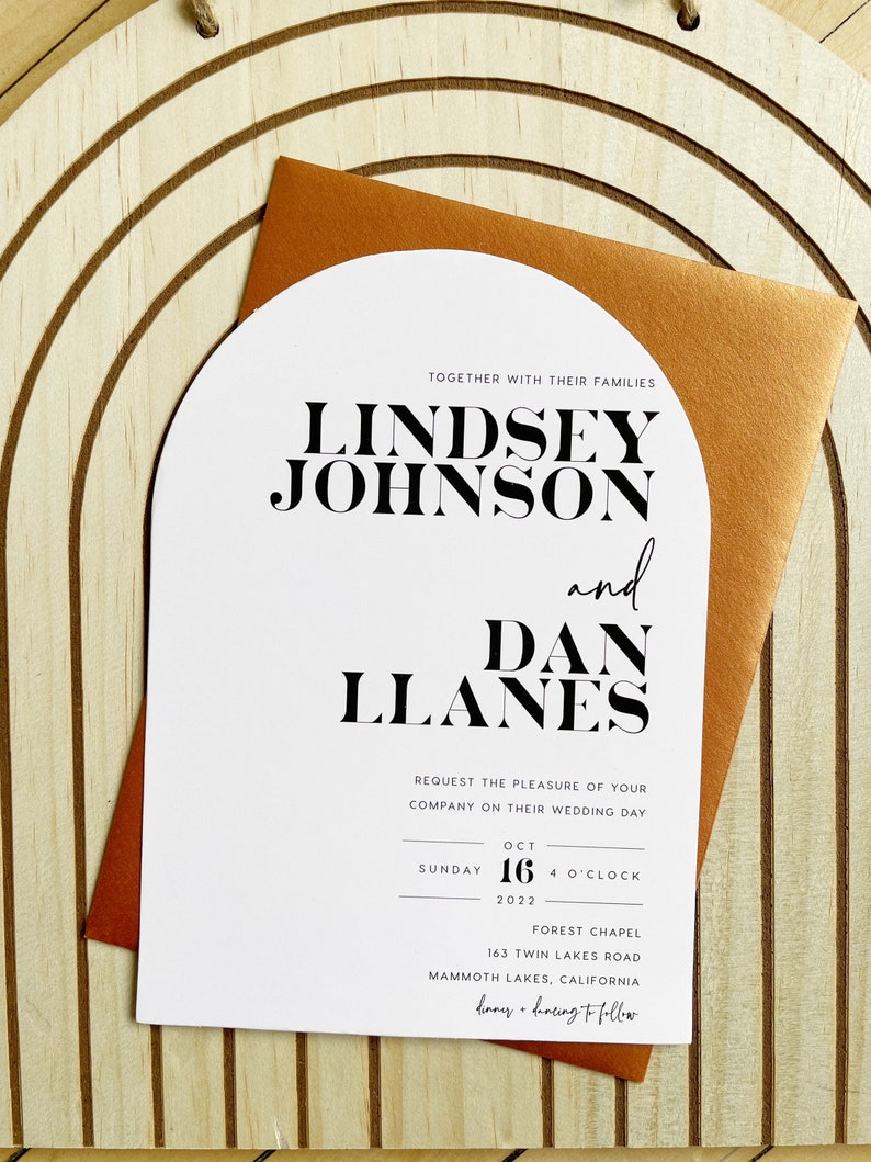 May include: A white wedding invitation with a modern arch design. The invitation features the names Lindsey Johnson and Dan Llanes in bold black text. The wedding date is October 16, 2022, at 4 o'clock at the Forest Chapel, 163 Twin Lakes Road, Mammoth Lakes, California.