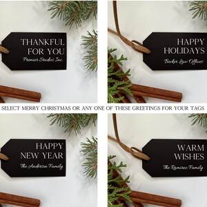 May include: Four black gift tags with white text. The tags are tied with brown twine and are displayed against a white background with sprigs of greenery. The text on the tags reads: "Thankful for you", "Happy Holidays", "Happy New Year", and "Warm Wishes".