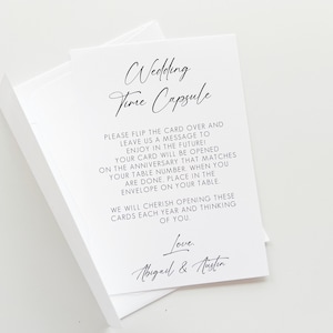 Puede incluir: Una tarjeta blanca con texto negro que dice "Wedding Time Capsule". La tarjeta instruye a los invitados a escribir un mensaje para la pareja para abrir en su aniversario.