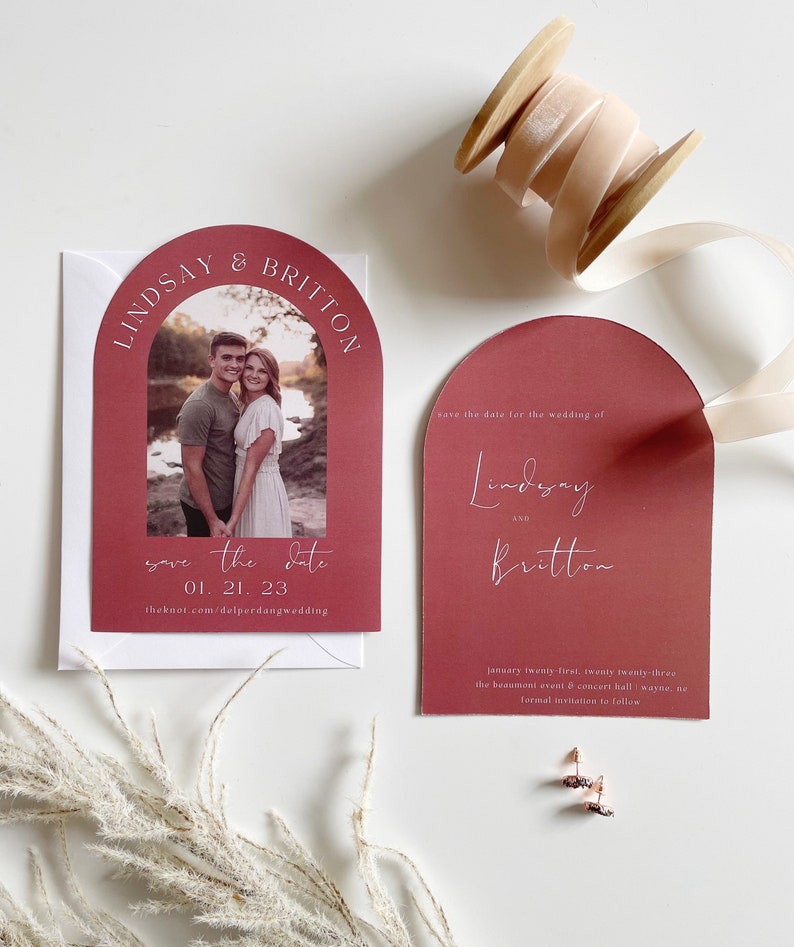 May include: Save the date card with a burgundy arch design. The card features a photo of a couple and the text "Save the date 01.21.23 theknot.com/delperdangwedding".