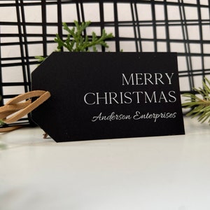 May include: Black gift tag with white text that reads "Merry Christmas" and "Anderson Enterprises".
