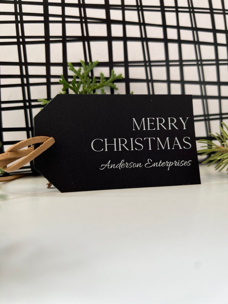 May include: Black gift tag with white text that reads "Merry Christmas" and "Anderson Enterprises".