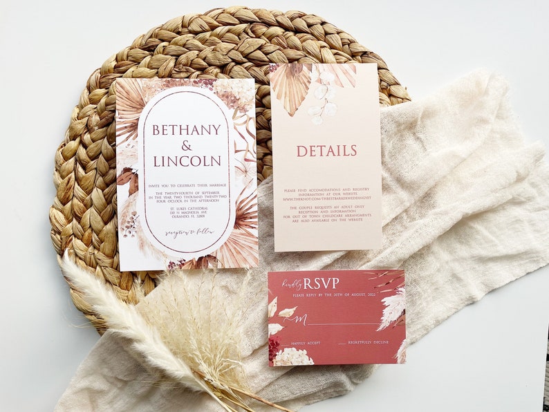 May include: A set of three wedding invitations with a boho theme. The invitations are printed on cream and blush colored cardstock with a floral design and the text "Bethany & Lincoln" and "Details". The RSVP card is red with a floral design and the text "Kindly RSVP".