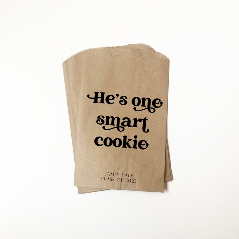 May include: Brown paper bags with the text "He's one smart cookie" printed in black. The bags also have the text "James Yale Class of 2023" printed in black.