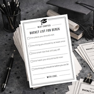 May include: A stack of white paper bucket list sheets with black text, including "Next Chapter" and "Bucket List for Derek." A black pen and a pencil holder with pens are on the left. A graduation cap is in the background.