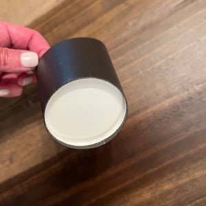 Op de afbeelding: Een zwarte kartonnen buis met een witte binnenkant. De buis wordt in een hand gehouden.