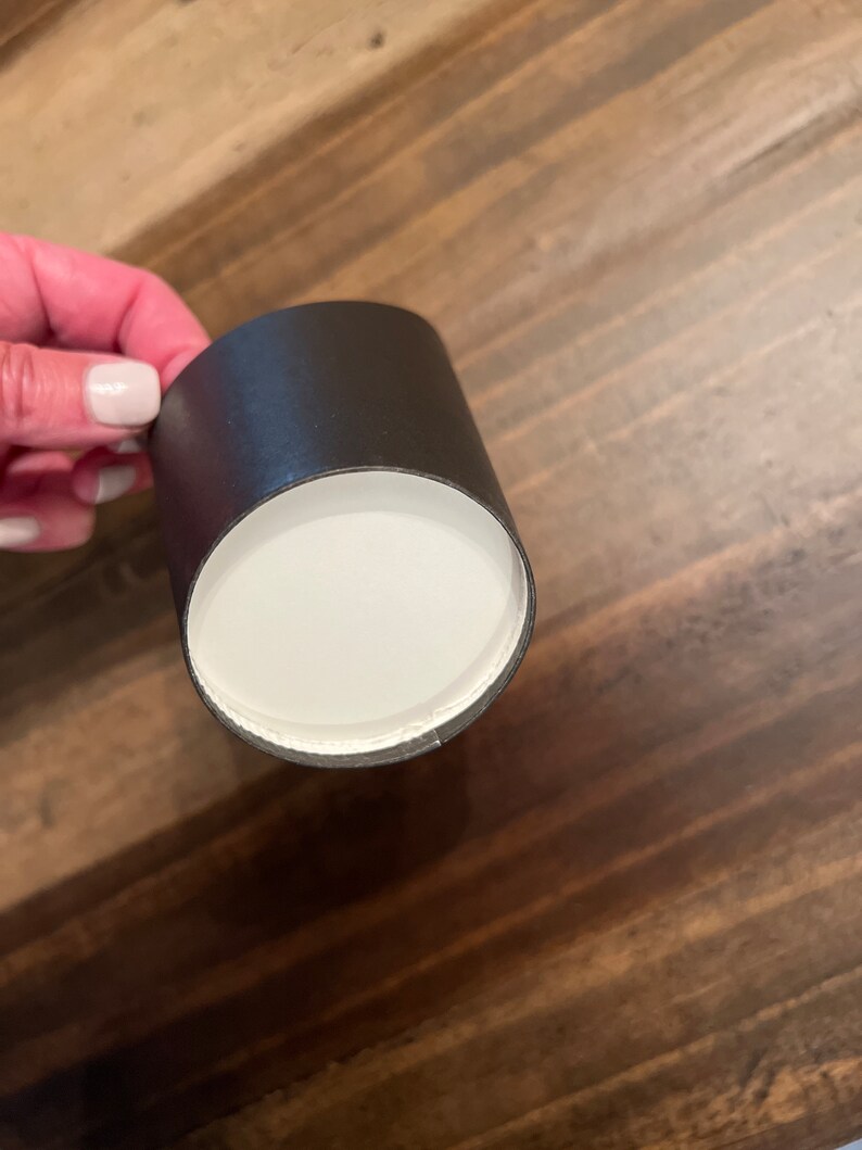 Op de afbeelding: Een zwarte kartonnen buis met een witte binnenkant. De buis wordt in een hand gehouden.
