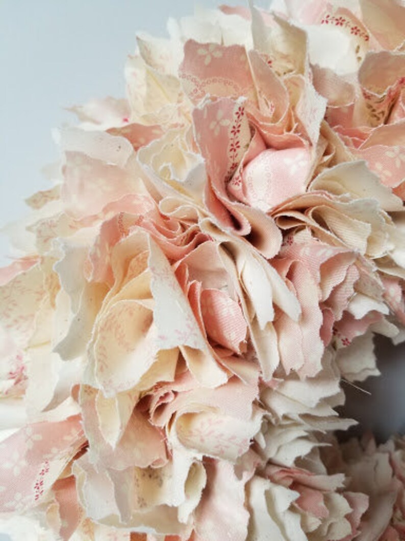 Puede incluir: Una corona hecha de retazos de tela en tonos rosa y blanco. La tela est&aacute; superpuesta y fruncida para crear un aspecto lleno y esponjoso.