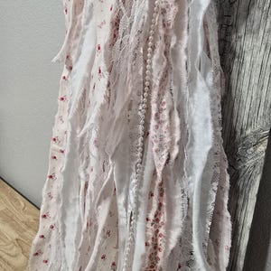 May include: A white and pink fabric garland with a string of pearls. The fabric is frayed and has a floral pattern.