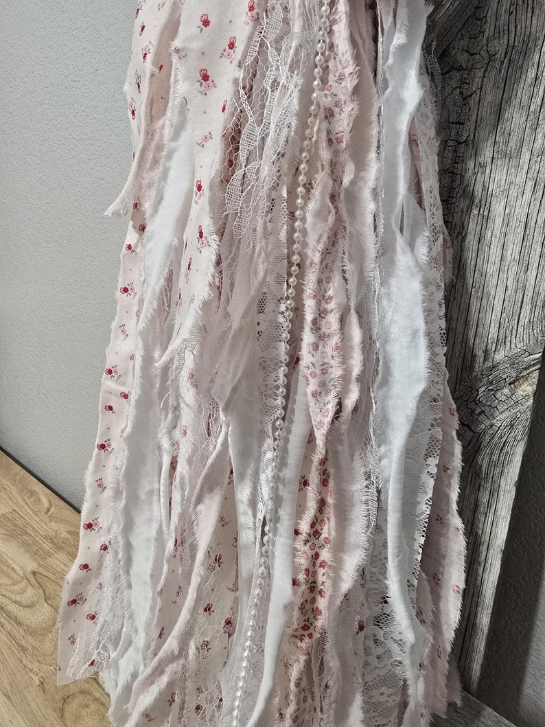 May include: A white and pink fabric garland with a string of pearls. The fabric is frayed and has a floral pattern.