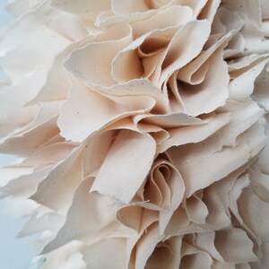 May include: A close-up of a white fabric wreath, made of multiple layers of fabric, creating a ruffled and textured effect.