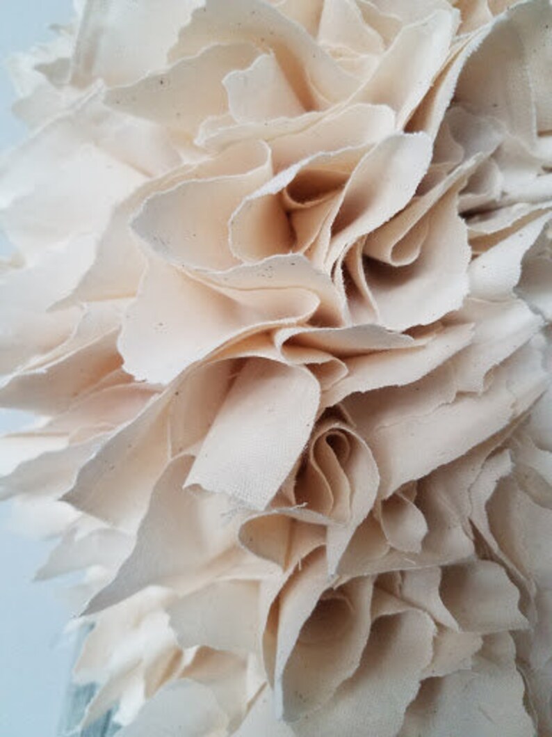 May include: A close-up of a white fabric wreath, made of multiple layers of fabric, creating a ruffled and textured effect.