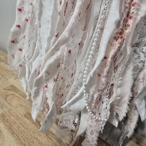 May include: A white and pink fabric garland with a pearl strand. The fabric is cut into strips and has a floral pattern.