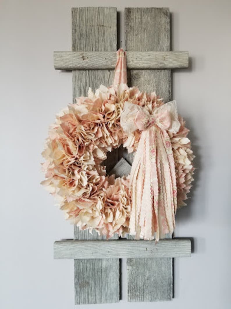 Puede incluir: Una corona de tela rosa y blanca con un lazo de tela rosa y blanca colgando de una estanter&iacute;a de pared de madera gris.