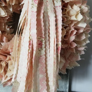 Puede incluir: Una corona de tejido rosa y blanco con una larga borla de tejido deshilachado que cuelga de la parte inferior. La borla est&aacute; hecha de m&uacute;ltiples tiras de tejido con un patr&oacute;n floral.