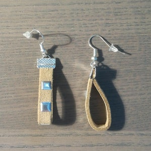 Peut inclure: Une paire de boucles d'oreilles en cuir marron avec des accents argentés. Une boucle d'oreille est rectangulaire avec trois clous argentés, tandis que l'autre est en forme de larme.