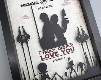 May include: A black framed shadow box featuring a layered paper cutout design with silhouettes of two figures, starships, and droids. The text reads MICHAEL, SHELLY, 08.08.2026, I TRULY, DEEPLY LOVE YOU, and EPISODE I against a weathered white background.