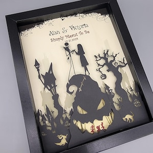 May include: A black framed paper art piece with a white background. The art features a silhouette of Jack Skellington and Sally from the Nightmare Before Christmas movie. The text "Alan & Victoria Simply Meant To Be 10.31.2023" is written in black at the top of the art.