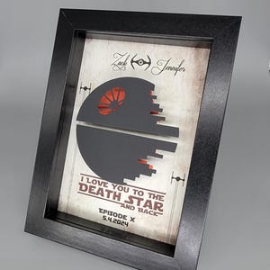 May include: A framed print with a black and red Death Star design. The print says "I love you to the Death Star and back - Episode X 5.4.2024". The names "Zack" and "Jennifer" are written at the top of the print.