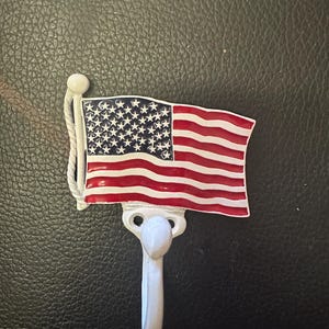 May include: White metal hook shaped like an American flag. The flag has red and white stripes and blue stars.