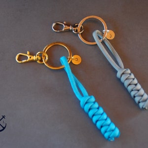 May include: Two keychains with braided cords and metal rings. One keychain has a blue cord and a gold ring with a letter "D" charm. The other keychain has a gray cord and a silver ring with a letter "J" charm.